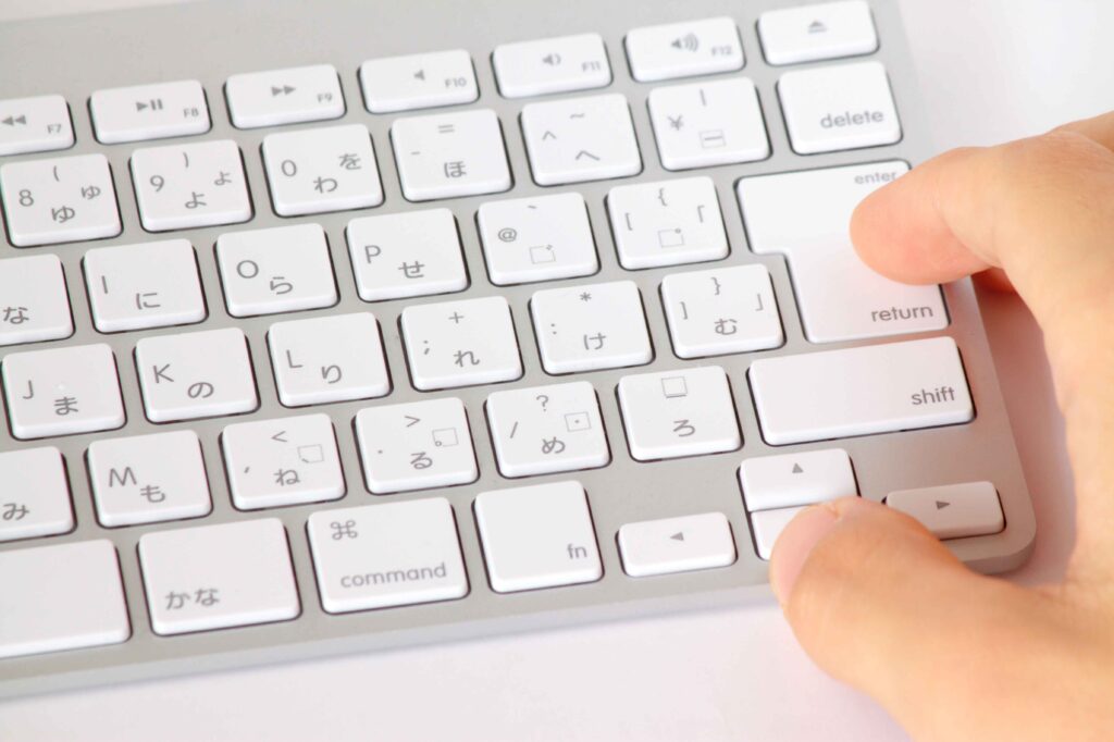 A closeup of a computer keyboard with Korean symbols alongside the Latin alphabet. A hand hovers ready to hit enter